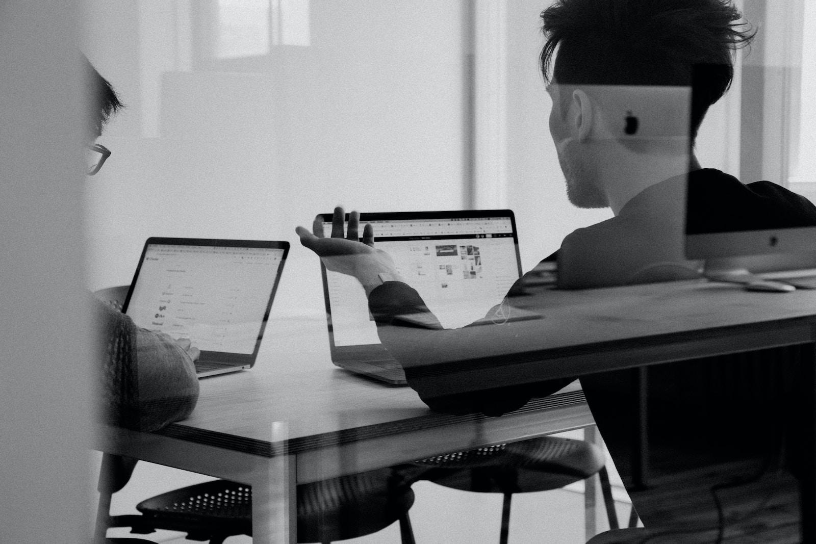 Schwarz-Weiß-Aufnahme von 2 Personen, die jeweils vor einem Laptop sitzen